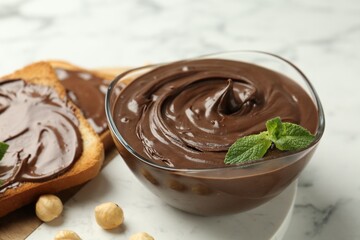 Tasty chocolate spread with mint and hazelnuts on white marble table, closeup