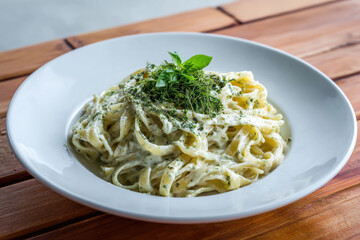 plate of creamy fettuccine alfredo on light table with focus on fresh basil sauce