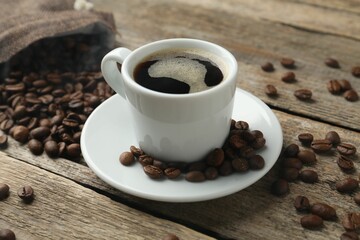 Aromatic coffee in cup and beans on wooden table, closeup
