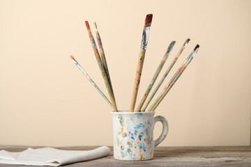 Brush with color paints in cup on wooden table