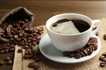 Aromatic coffee in cup and beans on table, closeup