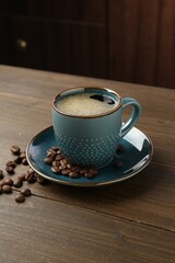 Aromatic coffee in cup and beans on wooden table, closeup