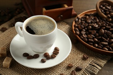 Aromatic coffee in cup, beans, brown sugar and grinder on table, closeup