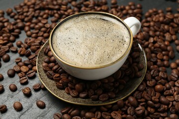 Aromatic coffee in cup and beans on black table, closeup