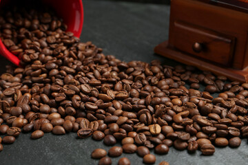 Aromatic coffee beans and grinder on black table, closeup