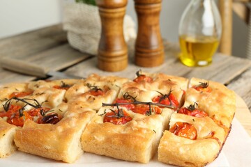 Cut delicious focaccia with tomatoes and spices on table, closeup