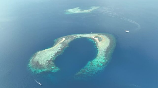 Seen from a bird's eye view, a picturesque atoll is found in the Molucca Sea near the island of Halmahera, Indonesia. Atolls form as the volcanic islands they surround slowly sink over geologic time.