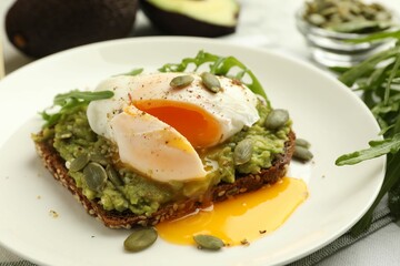 Delicious sandwich with avocado, poached egg, arugula and pumpkin on table, closeup