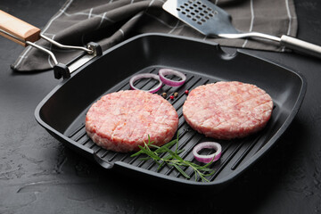Fresh raw patties for burger and spices in frying pan on black table, closeup