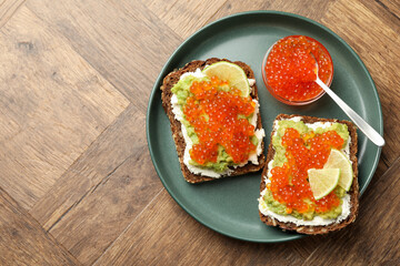 Delicious sandwiches with avocado, red caviar, cream cheese and lime on wooden table, top view. Space for text