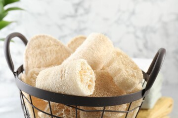 Different loofah sponges in basket and towels on table, closeup