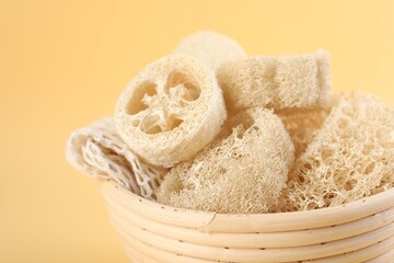 Different loofah sponges in bowl on beige background, closeup