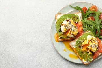 Delicious sandwiches with avocado, poached egg, salmon, tomatoes and arugula on gray table, top view. Space for text