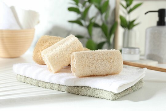 Different loofah sponges and towels on white table, closeup