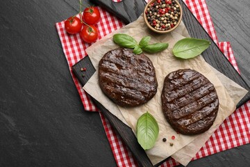 Delicious hamburger patties, tomatoes and spices on black table, flat lay. Space for text