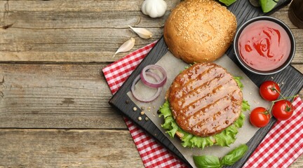Delicious hamburger patty, bun, vegetables and spices on wooden table, flat lay. Space for text