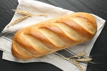 Loaf of bread and spikes on black textured table, flat lay