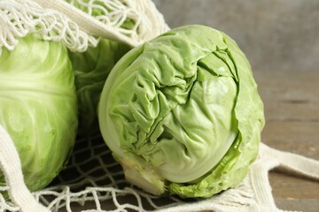 Fototapeta premium Fresh cabbages and net bag on wooden table, closeup