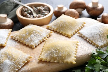 Uncooked ravioli and mushrooms on black table, closeup