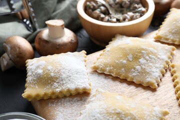 Uncooked ravioli and mushrooms on black table, closeup