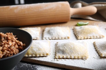 Uncooked ravioli, rolling pin and bolognese on black table, closeup