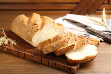 Cut bread loaf, spikelets and knife on wooden table, closeup
