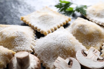 Uncooked ravioli, parsley and mushrooms on black table, closeup