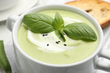 Tasty pea cream soup with basil served on white table, closeup