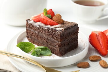 Piece of delicious chocolate cake with strawberry, almonds, mint and tea on table, closeup