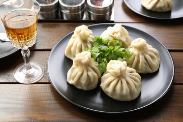 Delicious khinkali served with cilantro and wine on wooden table, closeup