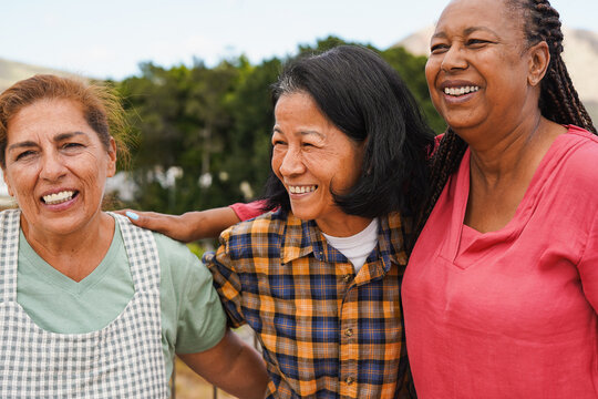 Happy multiracial senior women having fun together outdoor while hugging each other - Elderly female friendship and lifestyle concept