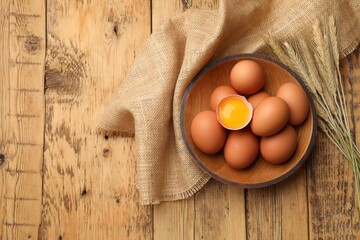 Fresh eggs, spikes and burlap cloth on wooden table, flat lay. Space for text