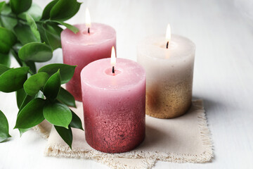 Burning candles and green leaves on white table, closeup