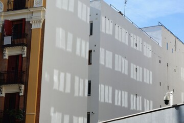 Morning sunlight casts intricate shadows of window frames on a white building