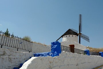 A traditional windmill with a thatched roof is surrounded by whitewashed walls and vibrant blue accents