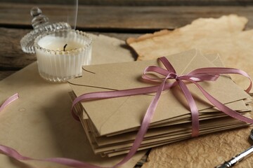 Stack of love letters, candle and parchment sheets on wooden table, closeup