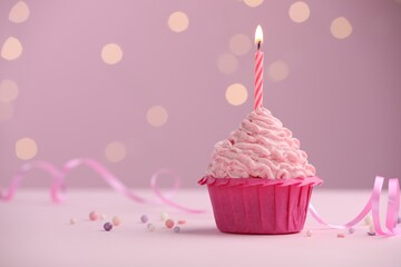 Burning candle in cupcake on table against pink background with blurred lights. Space for text