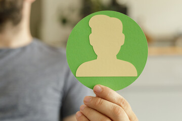 Hand holding a green circle with a beige person silhouette.  Represents profile, identity, user.
