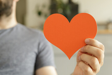 Close-up of a man holding an orange paper heart.  Perfect for love, romance, Valentine's Day.