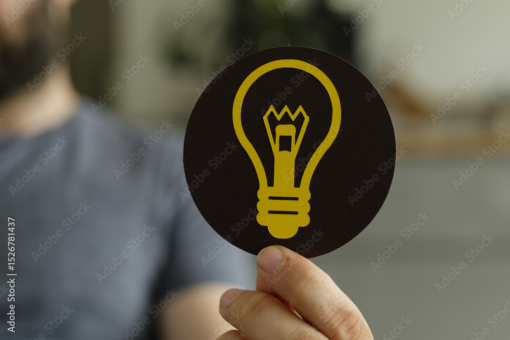 Poster a hand holds a circular card with a lightbulb symbol, representing ideas and innovation.