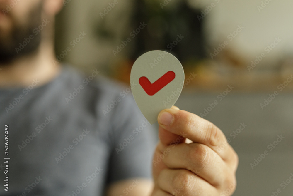 Poster close-up of a man's hand holding a grey paper location pin with a red check mark.