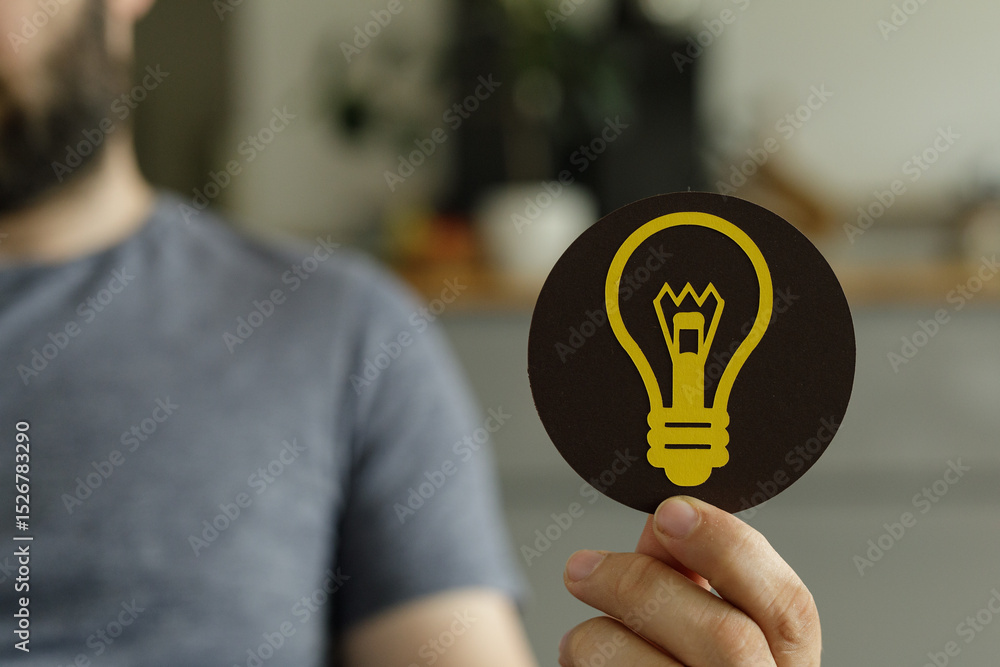 Poster a man holds up a round icon featuring a lightbulb, symbolizing ideas and innovation.