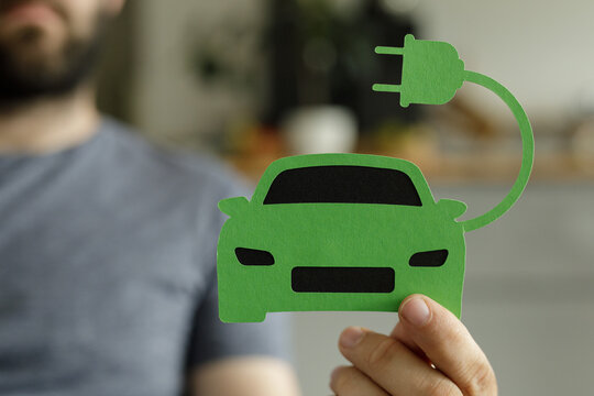 Fototapeta Image of a person holding a paper cut-out of an electric car, representing green transportation and sustainable energy.