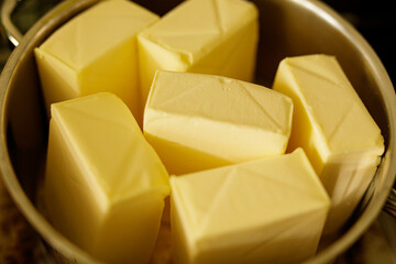 Close-up of creamy yellow butter cubes melting in a metal bowl. Perfect for baking and cooking.