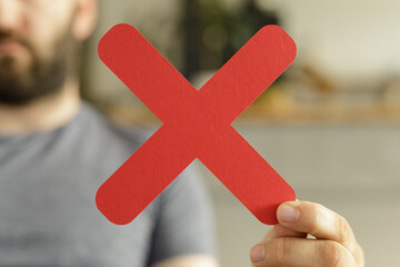 A man holds a red X symbol, signifying rejection, cancellation, or denial.  Perfect for...