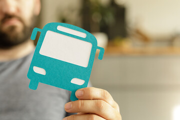 A man holds a teal paper bus cutout.  Public transportation, commute, travel concept.