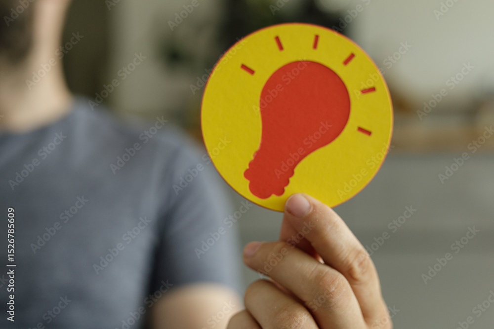 Poster a person holds up a circular sign featuring a lightbulb, symbolizing innovation and ideas.