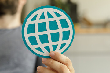 Stock photo of a person holding a teal paper cut-out of a world globe. Represents global...