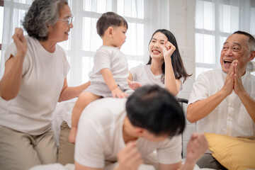 Fototapeta premium Joyful family gathering at home with grandparents, parents, and child sharing laughter and playful moments in the morning light
