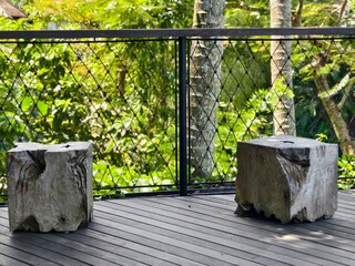 two rustic stools made from solid tree trunks on a wooden deck with a wire-mesh railing
